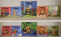 Top down view of 10 colorful Maki First Reader children's books arranged in two rows showing front cover and title illustrations featuring a cartoon dog.