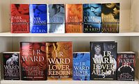 Photo of 12 J. R. Ward novels from Black Dagger Brotherhood series arranged in two rows on a white shelf. Includes three hardcover books and nine paperbacks.