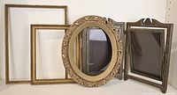 Five vintage wood frames including an ornate carved gold frame, two rectangular wood frames, and a hinged double standing frame arranged on white surface and leaning against a white shelf