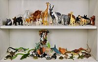 Photo shows two white shelves containing a variety of medium to large and small animal toy figures including mammals, dinosaurs, reptiles, and marine animals.