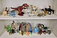 Full view of two shelves displaying an assortment of 27+ dinosaur toys, including large articulated figures on top shelf and smaller puppets and figures on lower shelf.