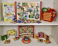 Photo showing assortment of educational toys including wooden maze puzzle with animal and word pieces, wooden letter flip board, VTech apple-shaped audio alphabet toy, My First Words puzzle book, and magnetic letters.