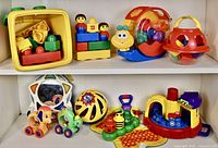 Shelf with a variety of toddler toys including Lego Duplo Primo blocks and figures, Fisher Price shape sorting toys, and other colorful plastic toys