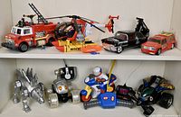 Front and side view of lot including red fire truck, yellow rescue helicopter, black vintage car, orange rescue SUV, and lower shelf with mechanical dinosaur, robot dog, motorcycle with rider and remote control, and other radio control vehicles.
