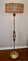 Full view of the floor lamp showing brass base, brass pole, teak accent, and interlaced wooden shade.