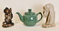 Photo displaying the old lady figurine, green tea pot and marble horse head paperweight on a white surface under good lighting.