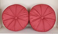 Front view of a pair of light red round decorative pillows showing pleated radial design and button center