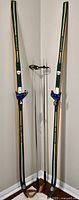 Front view of vintage green Gresshoppa cross country skis with bindings and metal ski poles with wooden handles leaning in a corner