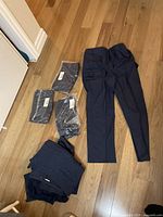 Eight pairs of women's plus size navy blue cargo pants laid out on wood floor, three unopened in plastic with labels