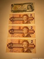 Front view of one $1 Canadian banknote and three $2 Canadian banknotes, Queen Elizabeth II portraits visible.