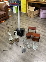Photo showing two white table lamps with brass accents, black dustpan with a white broom, HP 10bII calculator on floor, and three brown square wooden shelves in background.