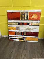 Front view of the painting showing its geometric design and color palette with reds, oranges, whites, blacks, and beige tones.