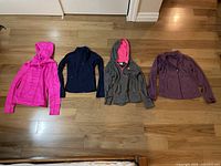 Four girls or teen hoodies and sweaters laid out on a wooden floor