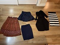 Five girls'/teen dresses and skirts laid out on floor showing variety of styles and colors.