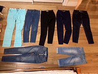 All 7 pairs of girl/teen pants laid out on a hardwood floor showing varying colors and styles