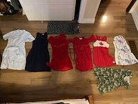 Eight girls' dresses laid out on wooden floor showing various styles and colors