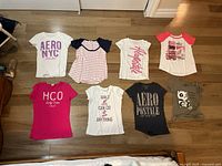 Top-down photo of eight girl's/teen's t-shirts laid flat, showing variety of colors, brands, and graphic styles.