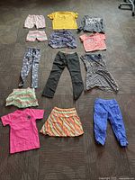 All clothing items spread out on the floor showing variety of tops, pants, skirts and shorts in multiple colors and prints