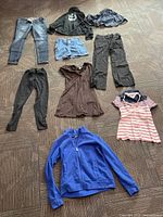 All clothing items laid out on floor, showing various garments including jeans, pants, skirt, dress, sweater, and tops.