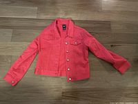 Front view of pink GAP girls denim jacket laid flat on wooden floor showing button front and long sleeves.