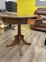 Round wooden table standing on wooden floor, drawer partly open showing dovetail joints, and round top surface visible.