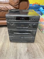 Front view of Sony mini hi-fi system showing cassette player, CD changer, and radio tuner display with control buttons.