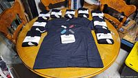 10 large black PAX T-shirts, one unwrapped and others wrapped in original packaging