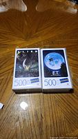 Two 500-piece jigsaw puzzles displayed on a wooden table, one featuring Alien artwork and the other E.T. artwork.