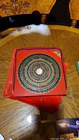 Decorative circular plate with Chinese characters and colorful concentric patterns on a red square base on wooden table.