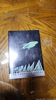 Front view of Futurama complete series DVD box set with spaceship design on black background.
