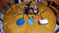 Top view showing the main press machine and four heating plates (round, rectangular, cylindrical) on a wooden table.