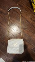 Full view of Michael Kors crossbody purse with chain strap laid flat on wooden floor.