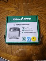 Packaged Rain Bird ESP-TM2 controller box showing product branding and features including WiFi capability, 4 stations, indoor/outdoor use.