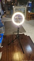 Photo showing the ring light illuminated on the adjustable tripod stand with integrated phone holder in garage setting.