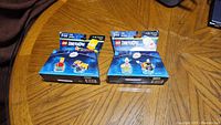Two LEGO Dimensions Simpsons Fun Packs displayed unopened on wooden table: Bart with Gravity Sprinter and Krusty the Clown with Clown Bike.