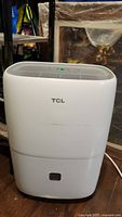 Front view of white TCL dehumidifier showing brand logo and water tank compartment.