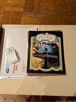 Photo showing the Grease promotional signed photo with USPS Priority Mail packaging beneath it