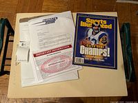 Photo showing the signed Sports Illustrated magazine and accompanying letter of authentication on a beige surface with some paperwork underneath.