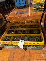 Top view photo showing the 16 champagne coupe glasses neatly arranged in a yellow plastic rack divided into individual sections for each glass.