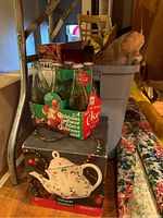 Photo showing Coca-Cola Christmas bottles in box next to Pfaltzgraff Winterberry teapot box and other holiday items on wood floor.