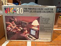 Front of the original Commodore VIC-20 box showing the branding, advertising text about the personal color computer with arcade game excitement, and an image of a family using the computer.