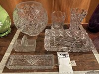Full view of assorted cut crystal items including a large bowl, two vases, a rectangular tray, small basket dish, and butter tray on a wood surface.
