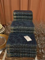 Sixteen volumes of Encyclopedia Judaica stacked on a table among glassware, showing the front and back of the books.