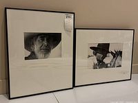 Wide shot of two framed black and white cowboy photographs displayed side by side on the floor against a wall.