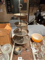 Godinger 3-tier silver plated stand with three round trays and handle, surrounded by other glassware and bowls.