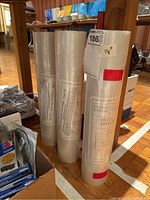 Three laminating film rolls standing upright showing their size and condition in a background of other office supplies and shelving.