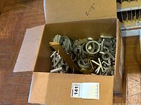 Cardboard box filled with assorted metal letters in silver and gold colors, sizes labeled 2-13 inches on the box flap