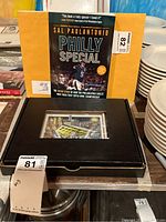 Hardcover book and framed 3D artwork in black presentation box with yellow envelope behind.