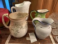 Four assorted ceramic pitchers including a milk glass pitcher, one with floral vine pattern and others with decorative painting