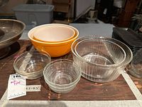 Overview of all bowls showing two orange mixing bowls, clear pleated baking bowls, and smaller clear finger bowls arranged on wood surface.